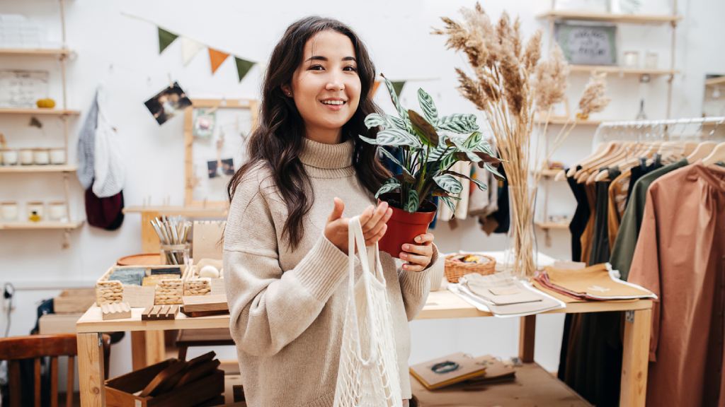 young woman smiling in ecological shop with eco-friendly products with a net bag and potted plant