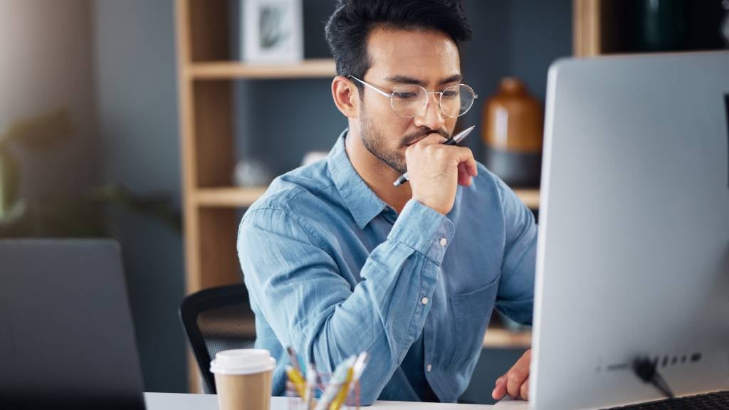 A man deep in thought sits at his desk and looks at his monitor