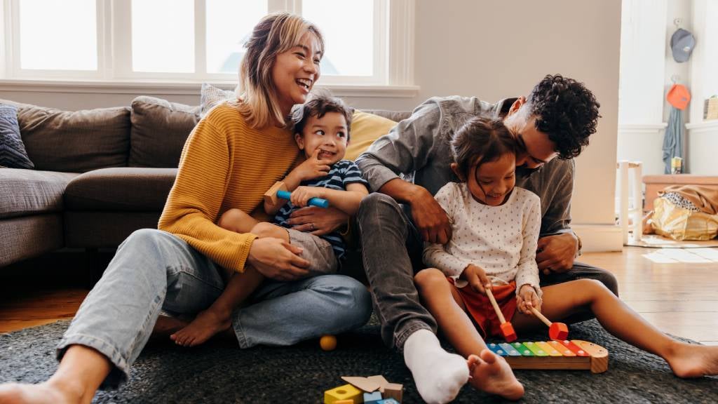 Young mum and dad play with their two children on their living room floor
