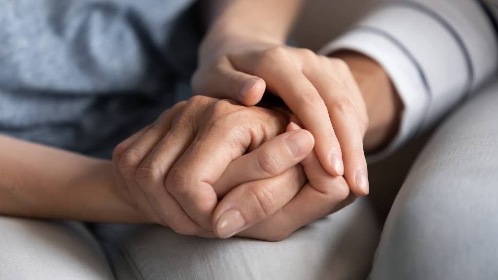 A young adult holding the hand of an older person to comfort them