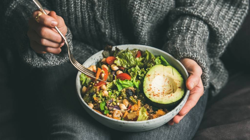 Woman in jeans and woollen jumper holding a bowl with a mix of healthy foods 