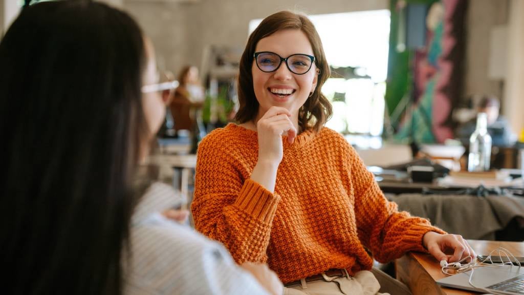 Two smiling colleagues sitting at their desk talking