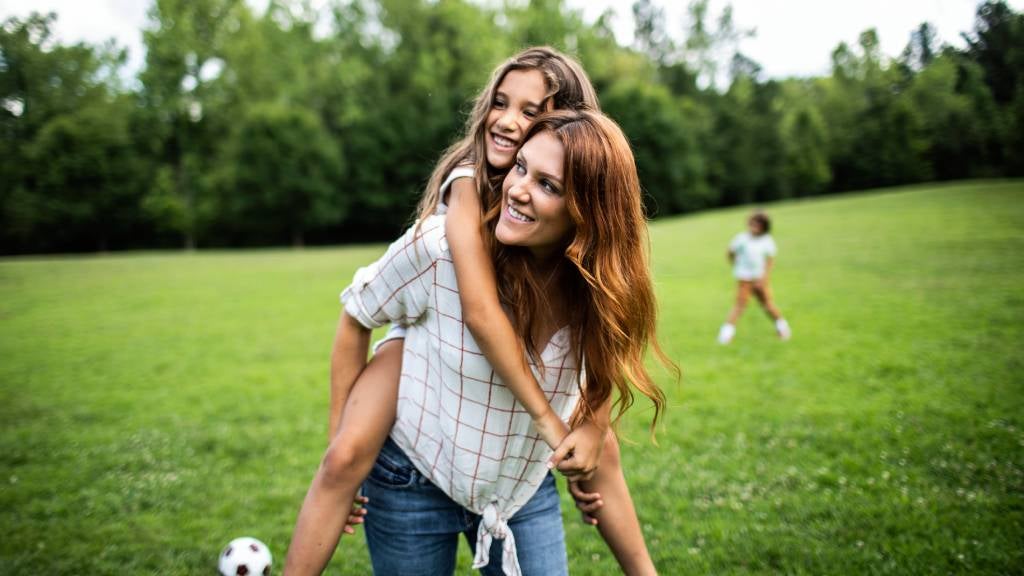 Daughter riding on her mother’s shoulders in park