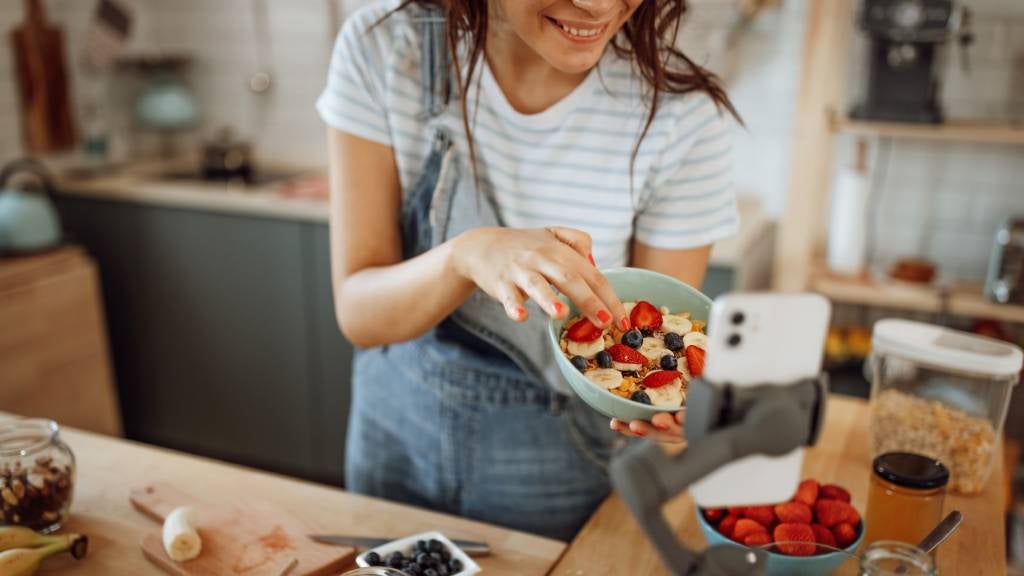 woman films herself preparing a berry breakfast bowl