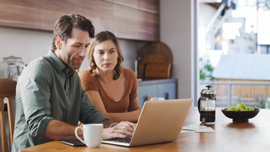 Couple sitting at kitchen table and looking at their laptop  