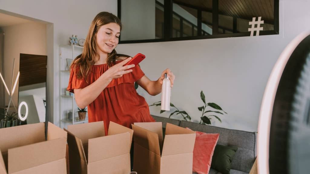 Female influencer using her phone to take a picture of her packing a product