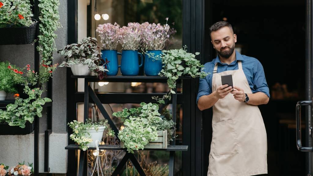 Smiling man views his phone near entrance of his plant nursery