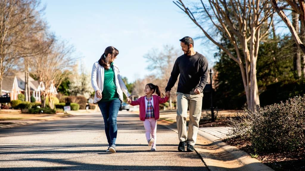 
Family Of Three Walking Through Suburban Neighborhood