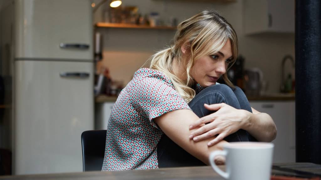 Woman sitting at the kitchen table with her legs tucked against her chest