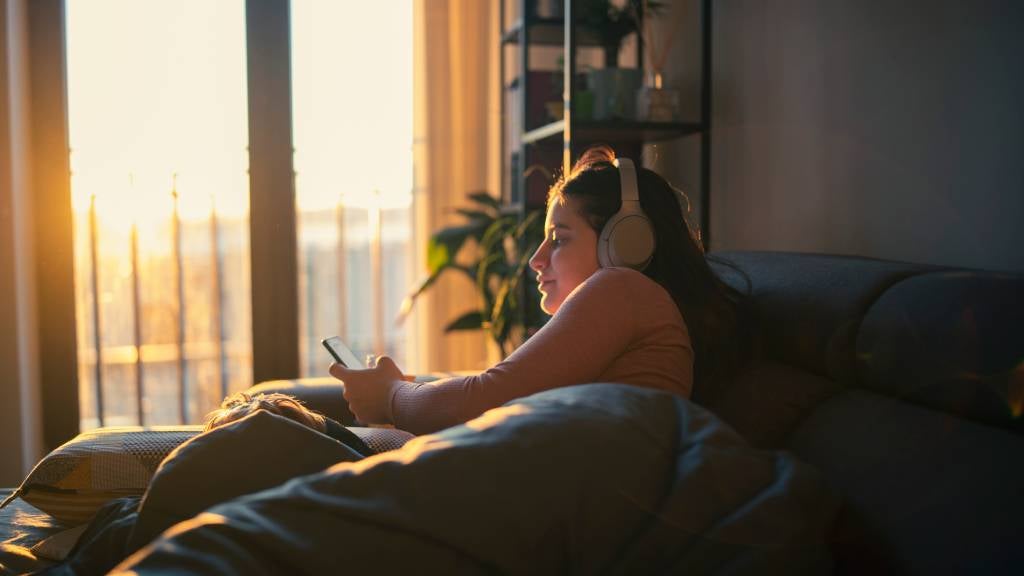 Woman laying on the couch listening to something on her phone through headphones