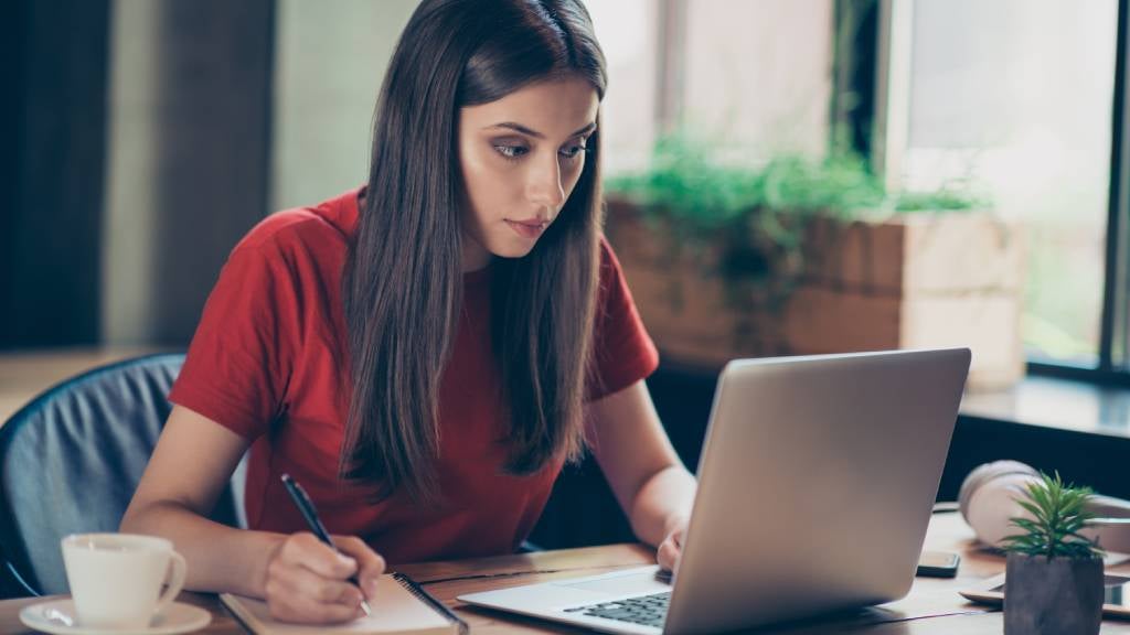 A woman looking at her laptop and making notes in her book