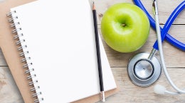 workbook, pen, apple and stethoscope on table