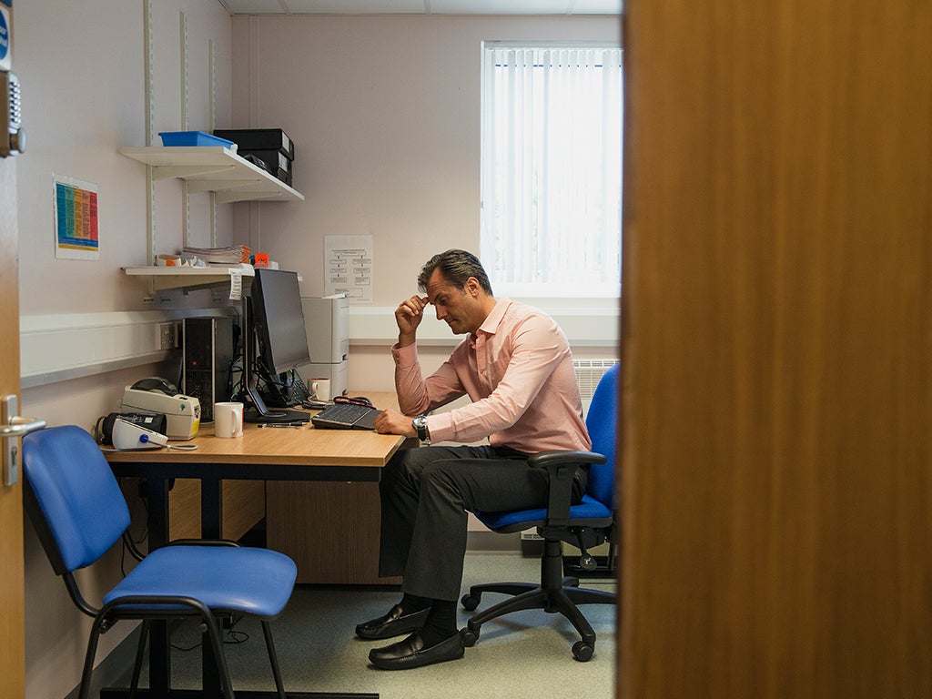 Male middle-aged doctor sitting at his desk looking down at the computer keyboard. 