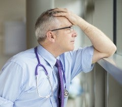 Doctor holding head in hand leaning on window