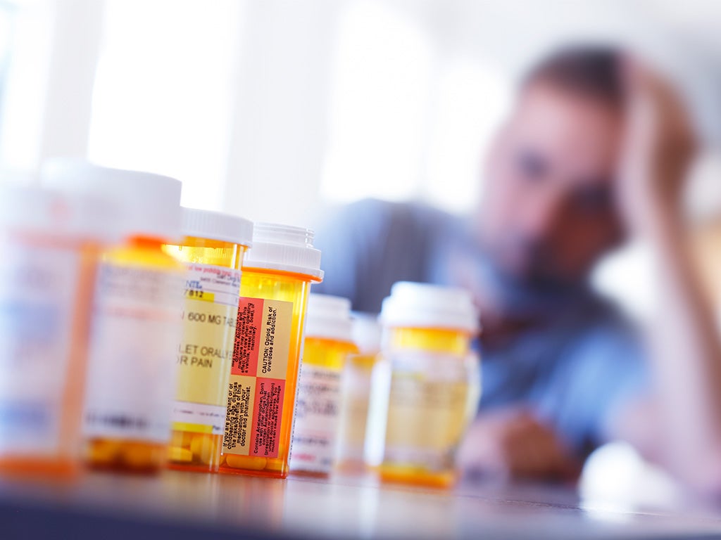 Man leaning on table looking a multiple medication bottles