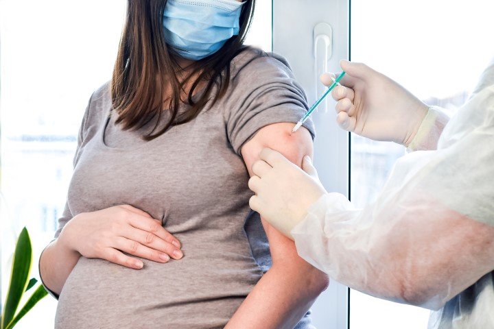 Woman with mask receiving vaccination into arm