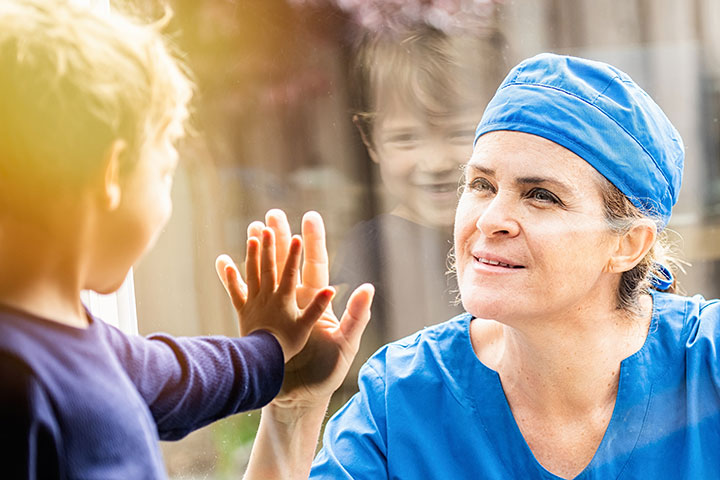 Healthcare worker placing hand on other side of glass to where child is placing hand
