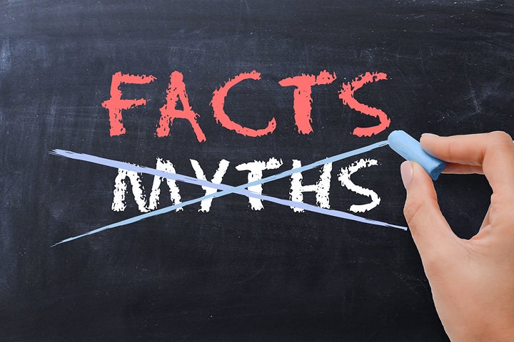 Image is of words on a blackboard with a hand holding blue chalk above it. On the black board the word Facts in red chalk is above the word Myths which is crossed out.