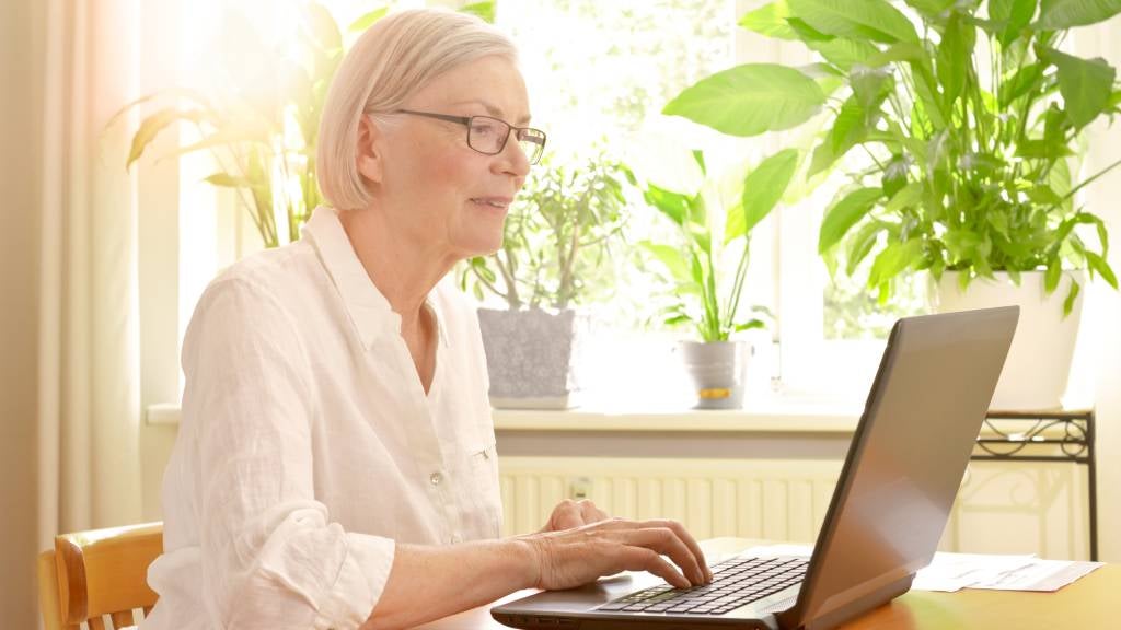 Senior woman in her sunny living room in front of her laptop