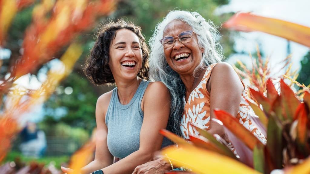 A smiling lady with silver hair and her teen granddaughter sit in a park