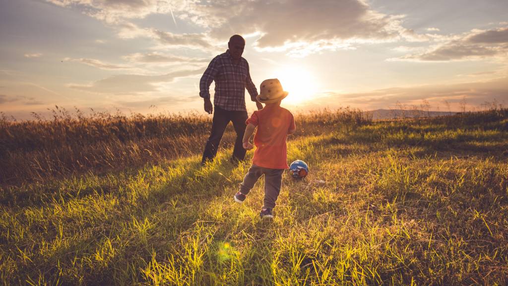 older man playing soccer outdoors with child