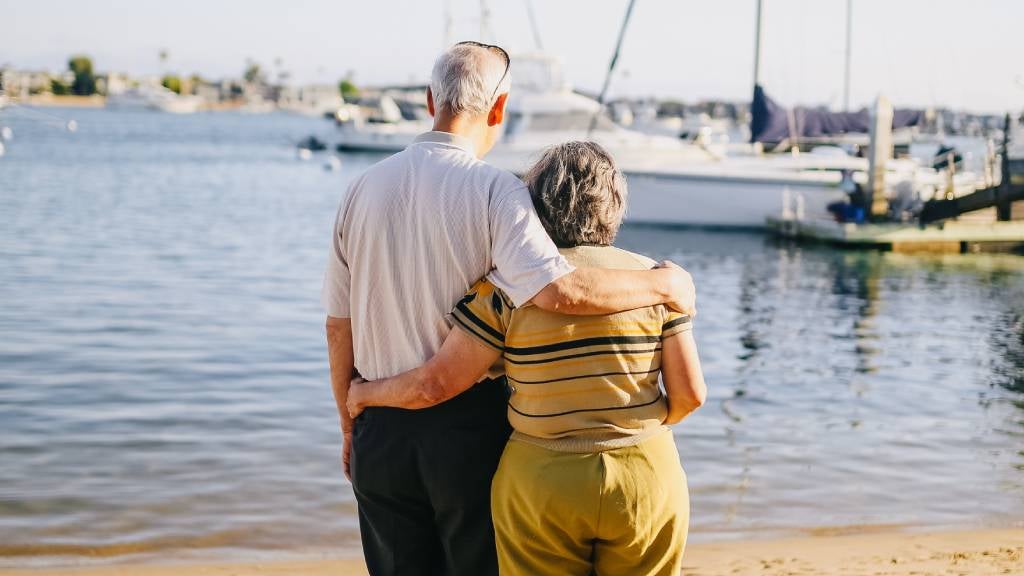 Senior couple pictured from behind standing near beach and yachts