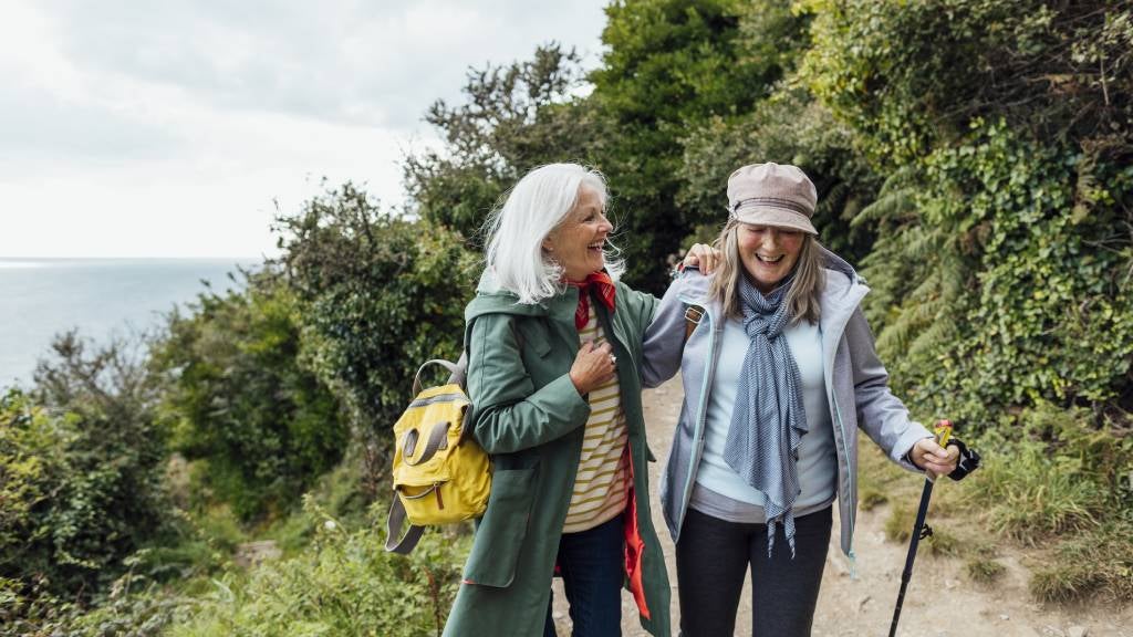 Two senior friends laughing and chatting while hiking together
