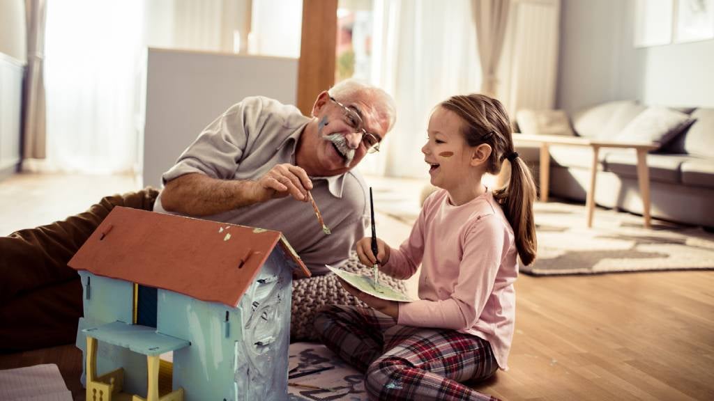 Grandfather and granddaughter laughing and painting doll house together.