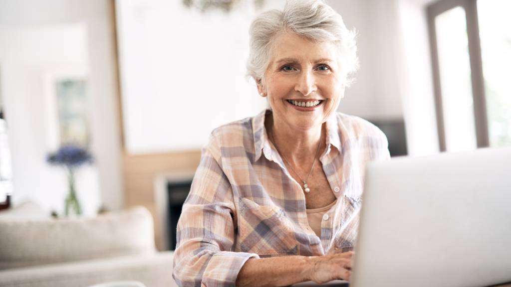 Senior lady sitting in front of a laptop smiling.
