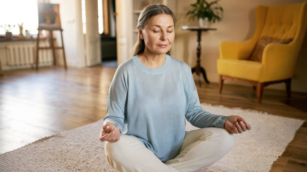 Senior female sitting on carpet doing mindful meditation 