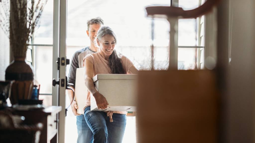 Couple in their 50s move into their new home, holding and unpacking boxes.