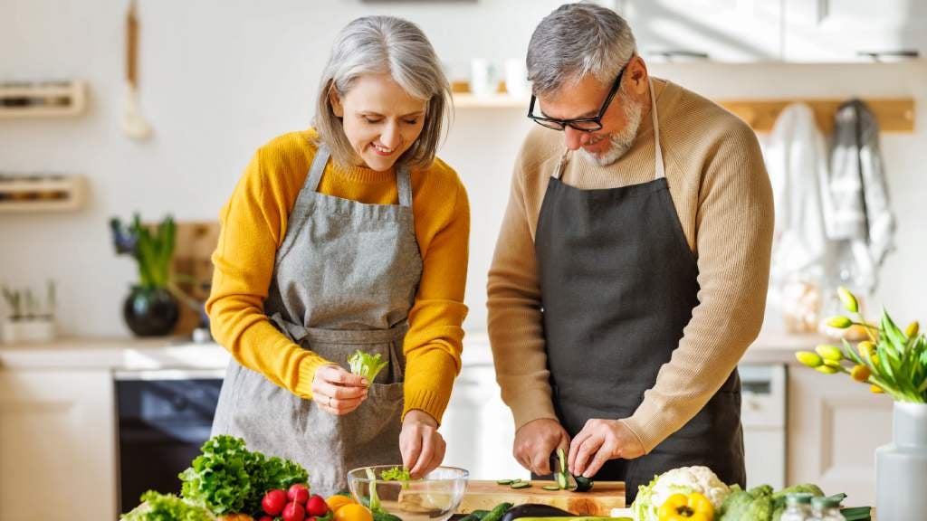 Happy elderly couple prepare dinner together, chopping fresh colourful vegetables