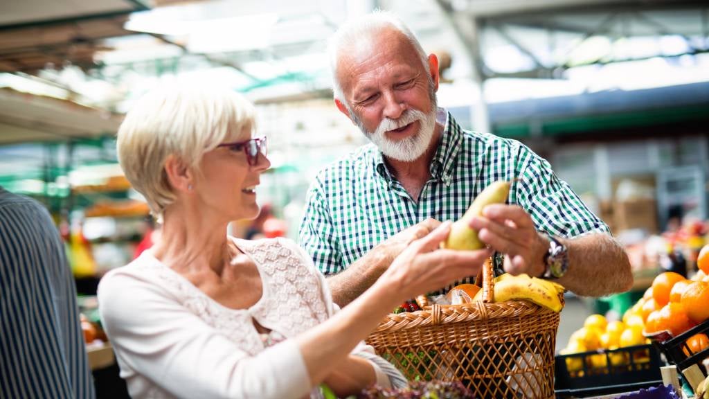 Senior couple in grocery aisle picking fruit and veg.