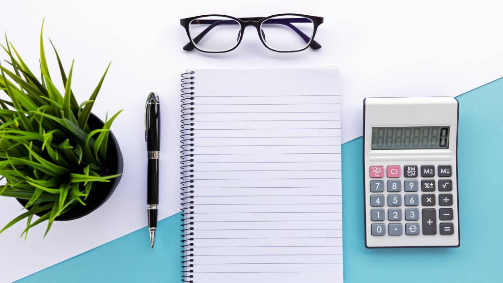 pen, paper, calculator and glasses on table to help manage a funeral insurance policy