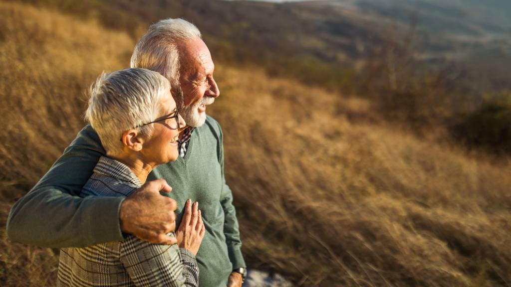 Senior couple hugging and overlooking view of city from a hill. 