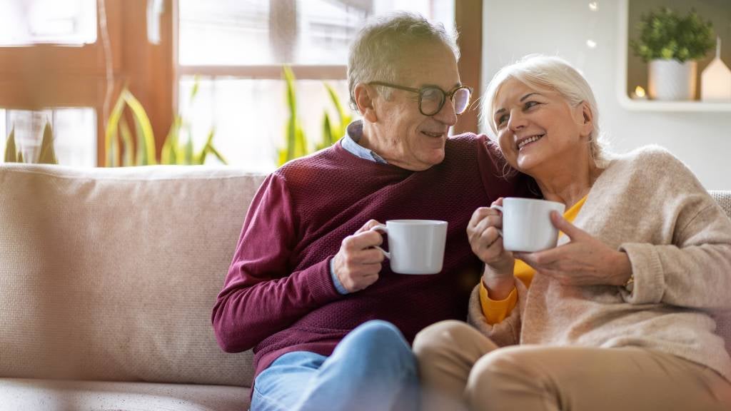 Senior couple sit on lounge together drinking a coffee out of a mug 