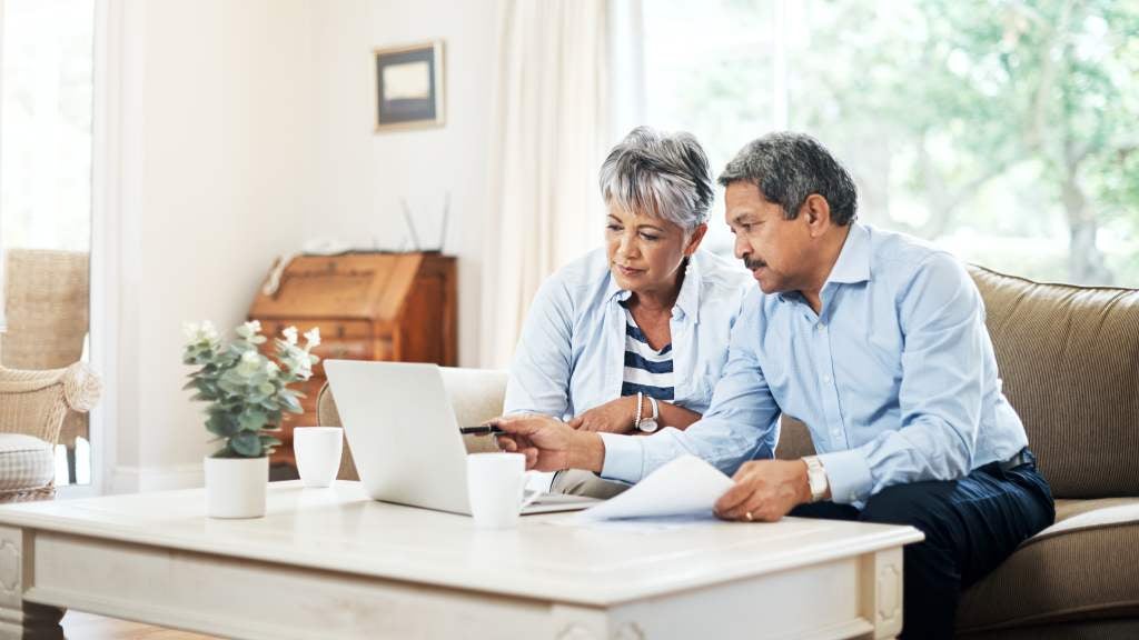 Couple sitting on the couch looking through documents and their computer.