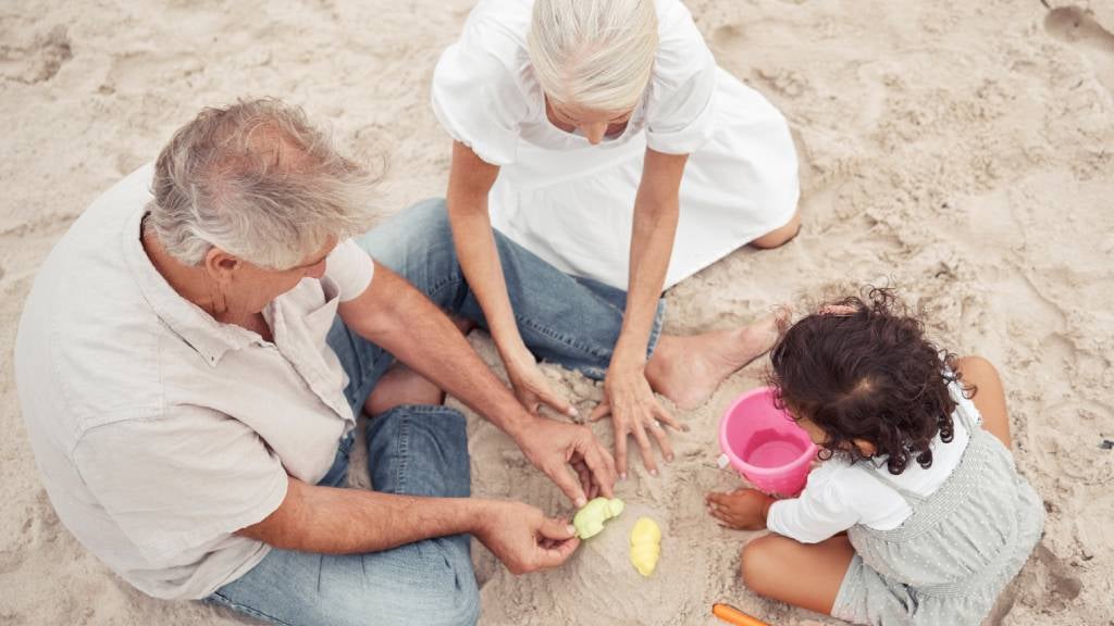 Grandparents playing in the sand with granddaughter at the beach