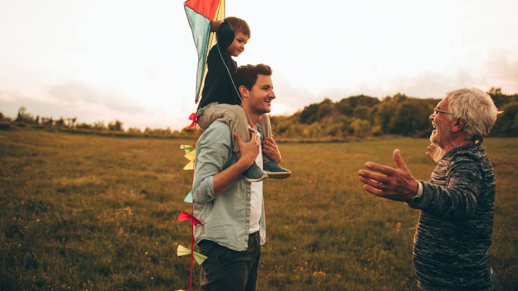 Grandfather with son and grandson flying a kite in the park.