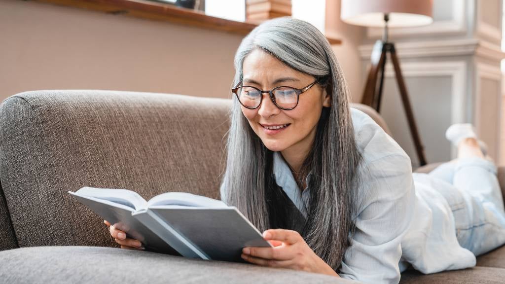 Senior woman relaxing and reading a book on the couch.