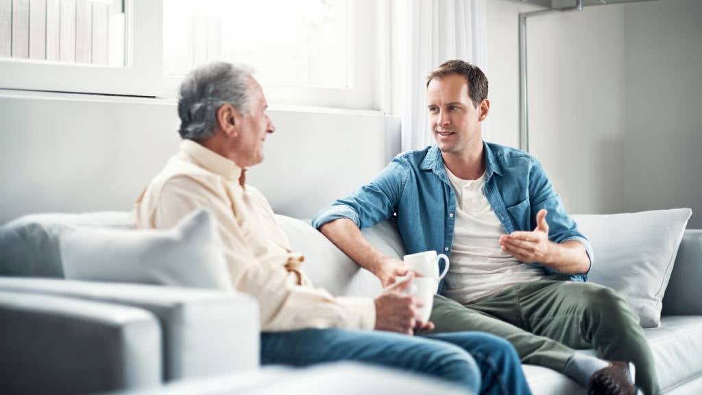 Father and son casually chatting on the couch with a cup of tea.