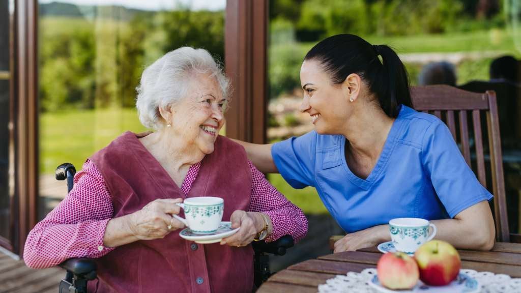 Woman having tea with female carer at new aged care home