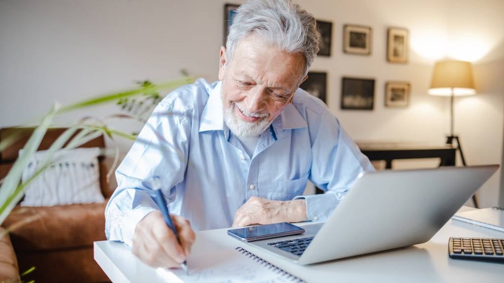 A senior man takes notes in his study