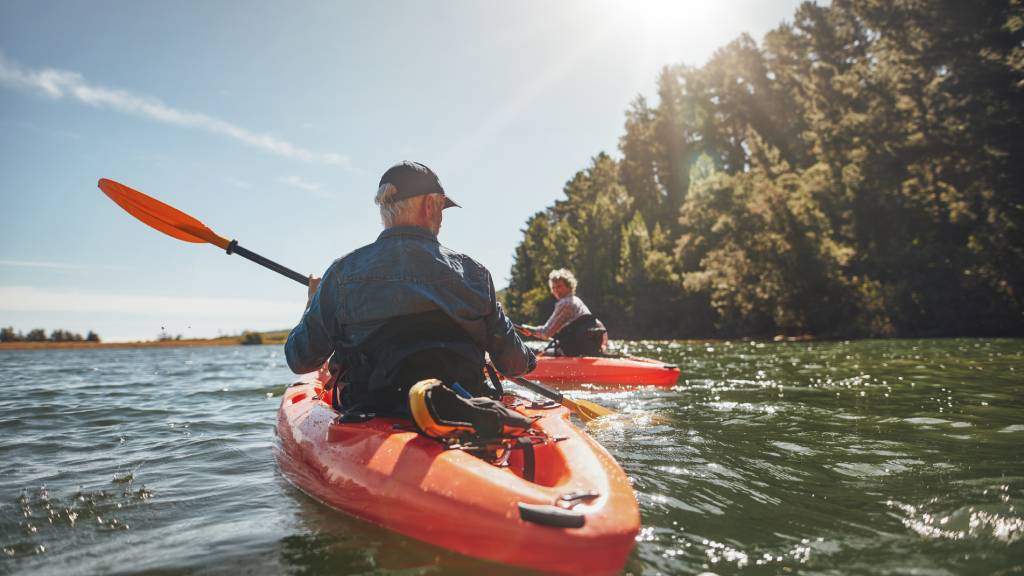 Older couple kayaking on a river with a red kayak 