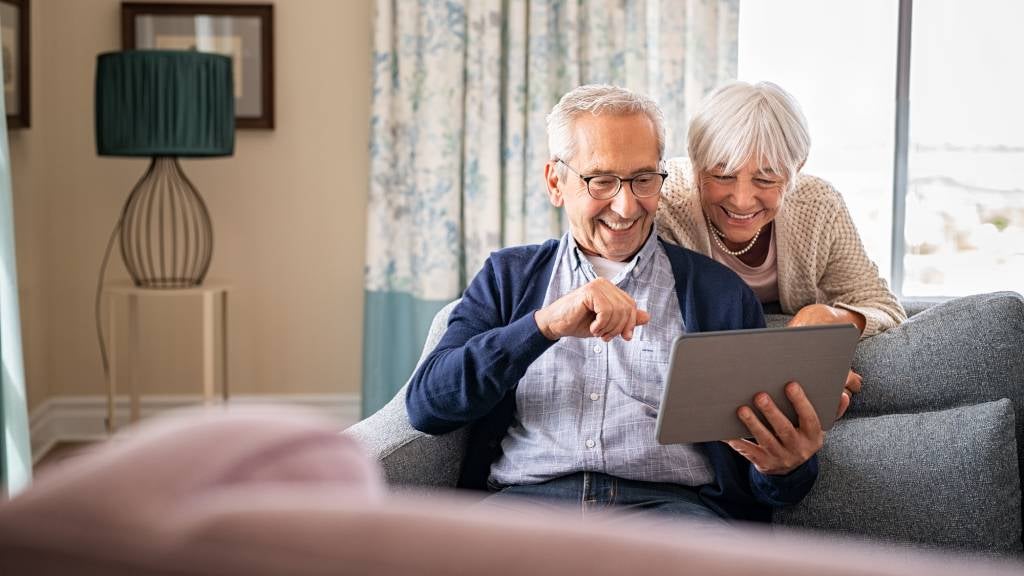 Happy senior couple looking at policies together on device 