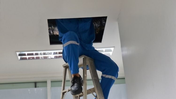 工人鑽入天花板維修孔維修管線