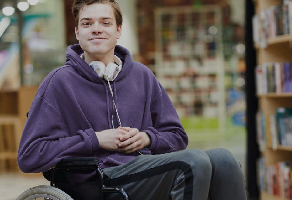 Physical Disability Council of NSW | Man with a disability sitting in a wheelchair in a library smiling at the camera | Devotion